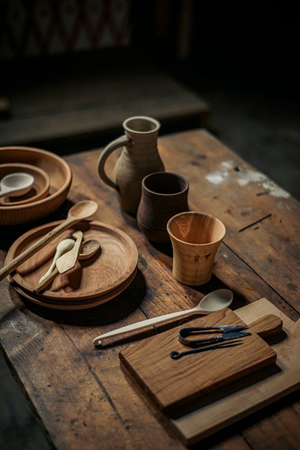 Handcrafted wooden kitchenware and pottery arranged on a wooden table.